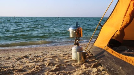 Camping stove with cooking pan  near tent on a sandy sea beach at the sunrise time