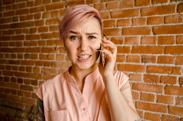 Young beautiful girl in perplexity is talking on the smartphone on a brick wall background