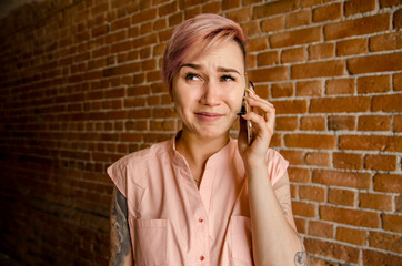 Young beautiful crying girl is talking on the smartphone on a brick wall background