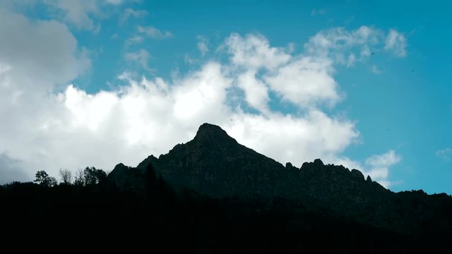 Clouds move through the huge rocky top of a large mountain. Timelapse 4K.