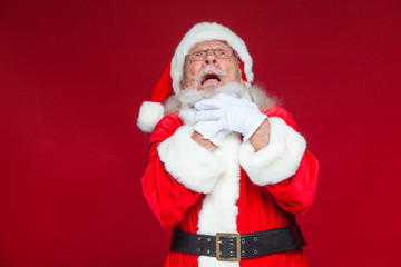 Christmas. Good Santa Claus in white gloves shows faces, grimaces, shows his tongue. Not standard behavior. Isolated on red background.