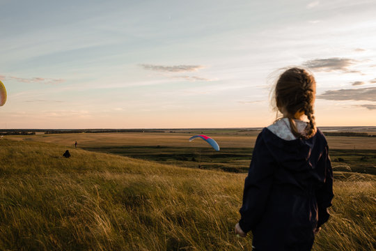 Little girl looks on soaring another paraplanes in sky