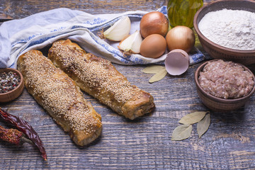 Homemade natural freshly baked strudel with forcemeat and ingredients for baking on a wooden table.