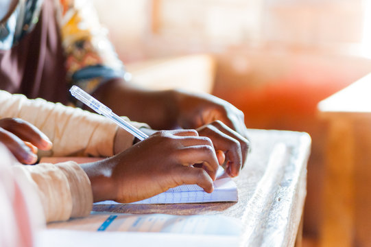 Hands Of Young African School Boys And Girls During Lesson In Classroom With Bright Sun Light Holding Pen And Writing