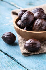 Whole inshell nutmeg nuts in a bowl on blue rustic wooden table.