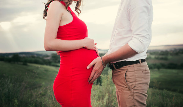 Close up of human hands holding pregnant belly, closeup happy family awaiting baby, standing on green grass, body part, young family and new life concept