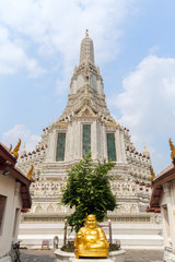 Fototapeta premium Golden statue of sitting Buddha and decorated Wat Arun temple viewed from the front in Bangkok, Thailand, on a sunny day.