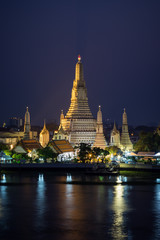 Fototapeta premium Beautiful view of lit Wat Arun temple next to Chao Phraya River in Bangkok, Thailand, in the evening.