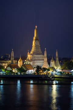 Beautiful view of lit Wat Arun temple next to Chao Phraya River in Bangkok, Thailand, in the evening.