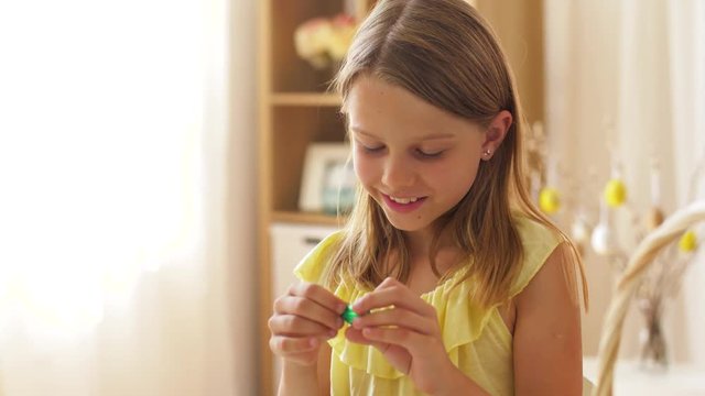 easter, holidays and people concept - happy girl removing wrapper from chocolate egg candy at home