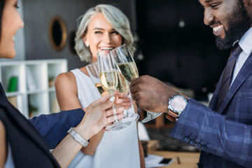smiling multiethnic businesspeople clinking with glasses of champagne in office