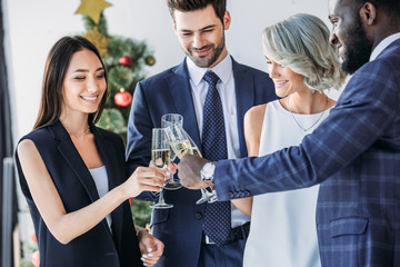multiethnic businesspeople clinking with glasses of champagne with christmas tree on background in office