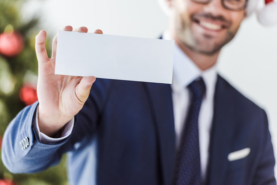 cropped image of businessman holding blank card in office with blurred christmas tree on background