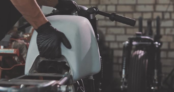 Auto mechanic assembles custom motorcycle in his workshop. Guy create an exclusive motobike cafe racer in the garage.