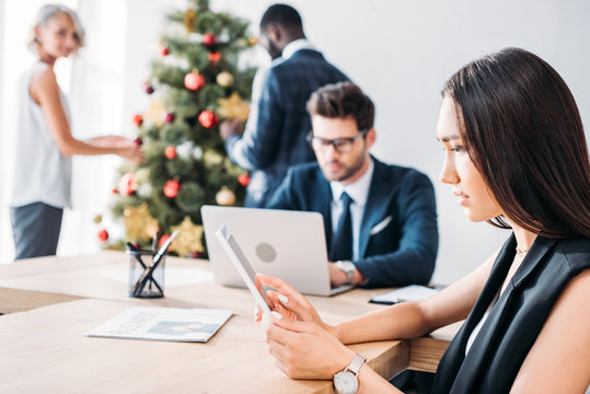 Asian Businesswoman Working And Colleagues Decorating Christmas Tree In Office