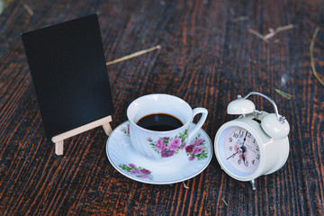 twinbell clock, cup of coffee, and mini blackboard on the wooden table. Image is concept of evening time