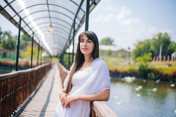 Beautiful girl with black long hair in a white dress on a bridge, walk near a pond. An orthodox woman