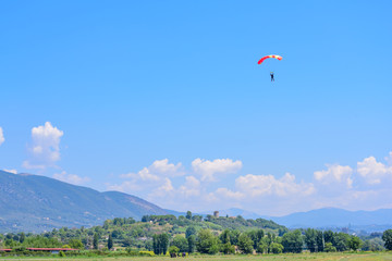 parachutist prepares for landing. On background the blue sky, mountains and green hills