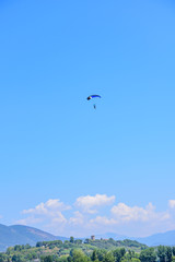 Fototapeta na wymiar parachutist prepares for landing. On background the blue sky, mountains and green hills