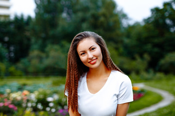 Naklejka premium Fitness and yoga concept. Positive girl in a white t-shirt and blue leggings doing yoga in the Park. Portrait of a smiling face on the background of nature. 