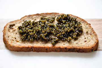 Slice of rye brown bread with black sturgeon caviar on a wooden cutting board closely. Elegant macro photo with expensive luxury delicatessen snack for party, bar, menu, cafe, restaurant, design