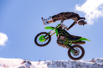 racer on a motorcycle in flight, jumps and takes off on a springboard against the snowy mountains