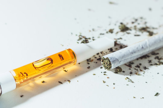 THC oil filled cartridge with rolled marijuana cigarette on white background