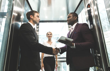 successful and young businessmen in the elevator business center rides to work. business handshake