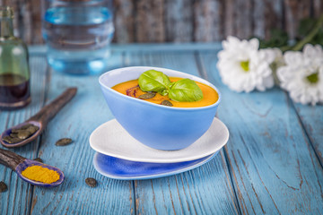 Pumpkin cream soup with pumpkin seeds, pumpkin oil and turmeric on a blue background