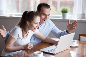 Millennial couple excited reading good news on laptop, happy man and woman screaming winning lottery online cannot believe eyes with success, spouses celebrate victory or achievement, feeling triumph