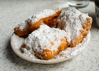 Fresh beignets come out of the fryer, topped with powdered sugar, ready to eat.