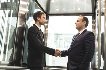 successful and young businessmen in the elevator business center rides to work. business handshake