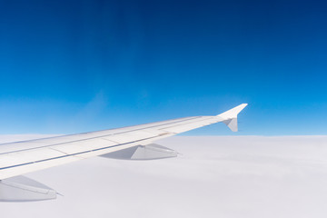 Wing of an airplane flying above the clouds. Window view of the blue sky. Aircraft wings.