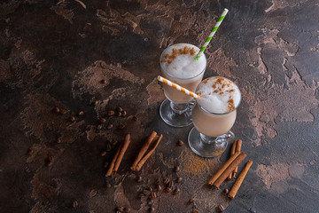 two glasses of latte on a wooden rustic table with coffee beans and cinnamon