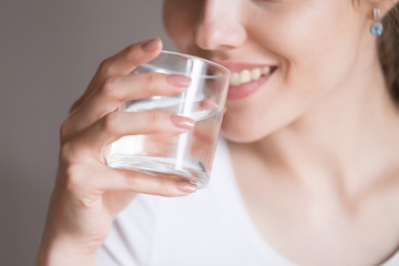 Close up of smiling woman feeling thirsty enjoying pure mineral water, dehydrated young female holding glass drinking aqua, girl taking care of own health. Concept of healthy lifestyle, good habit