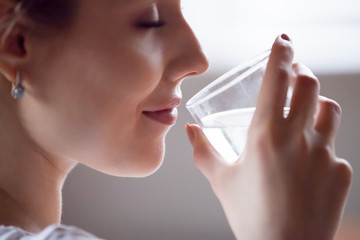 Close up of pretty female hold glass refreshing drinking pure mineral water in morning, thirsty...