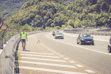 Panne auf der Autobahn: Junger Mann in gelber Warneweste stellt Pannendreieck zur Sicherung auf 