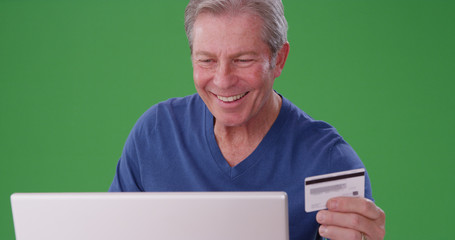 Senior caucasian male using credit card to pay online on greenscreen