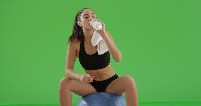 Hispanic girl drinking water sitting on exercise ball on green screen