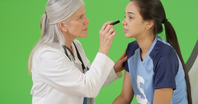 Young concussed soccer player is checked for dilated pupils on green screen