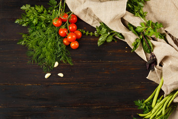 tomatoes, garlic,  beans and seasonal greens on wooden background with linen tablecloth (sackcloth), top view