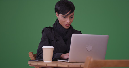 Fashionable woman using laptop computer at a cafe table on green screen