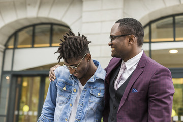 two young and stylish African American men in the city smiling and talking. father and adult son...