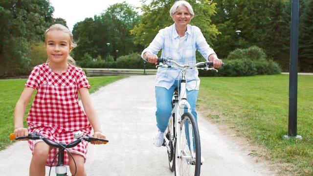 family, leisure and people concept - happy grandmother and granddaughter riding bicycles at summer park