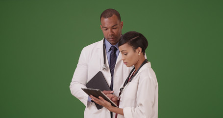 Two black doctors discuss their patient while on their tablets on green screen