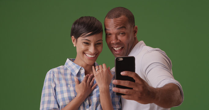 A black couple takes a selfie to celebrate their engagement on green screen