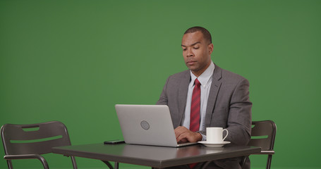 A black businessman with coffee works on his laptop on green screen