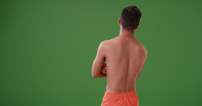 Rear view of Latino man in swimsuit looking out into distance on green screen