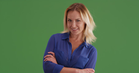 Woman in blue blouse with arms crossed smiling on green screen