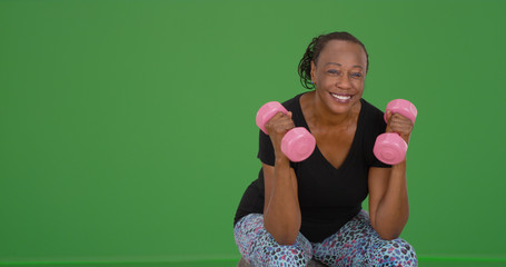 An elderly black woman lifts weights on green screen